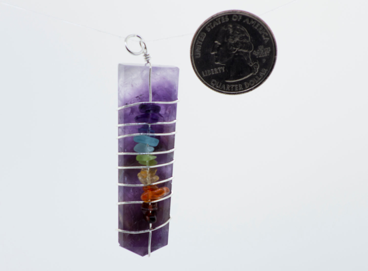 A Super Silver Wire Wrapped Tapered Slab With Chakra Stones pendant adorned with a coin.