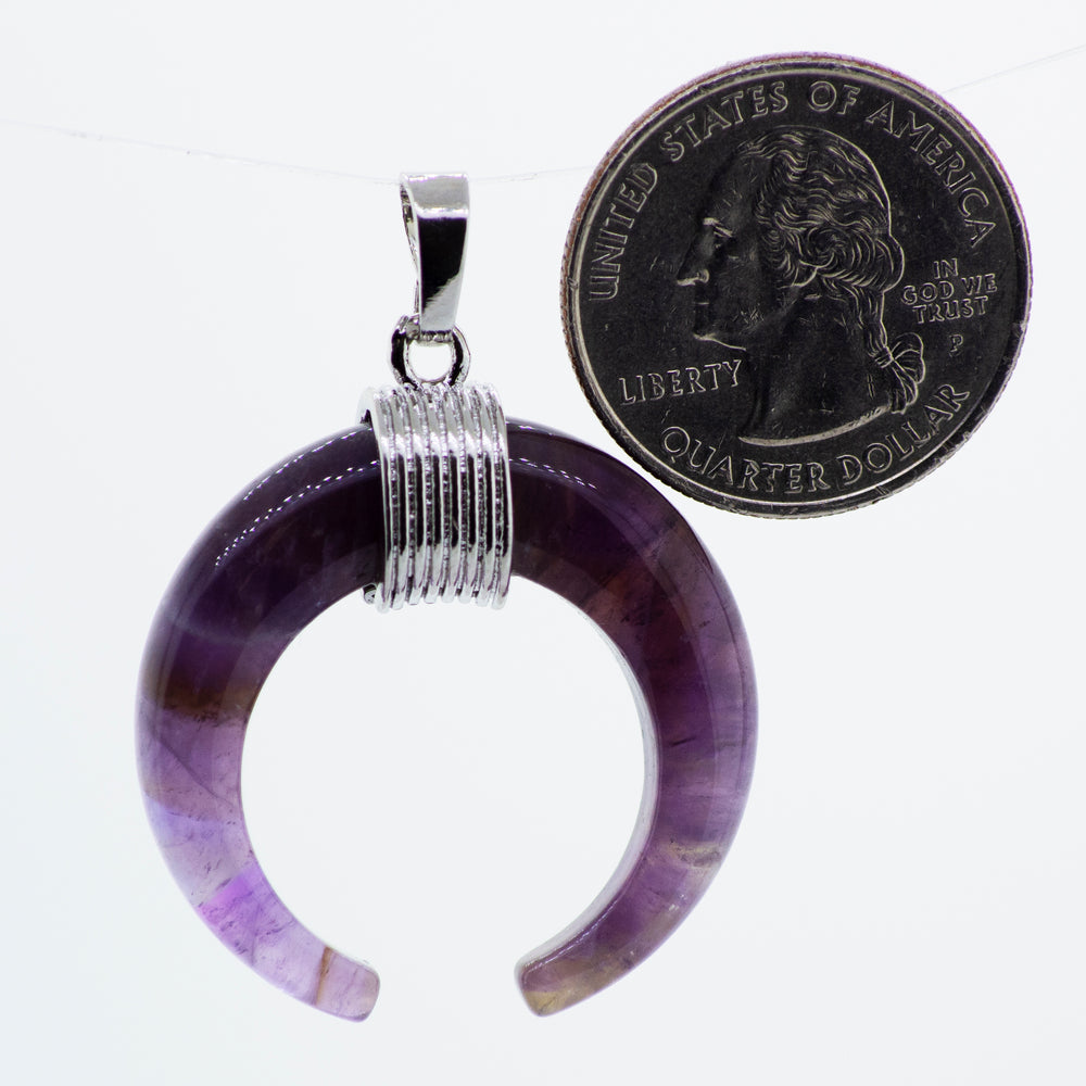 A Super Silver wire pattern setting holds a purple Naja Stone pendant with a coin hanging from it.