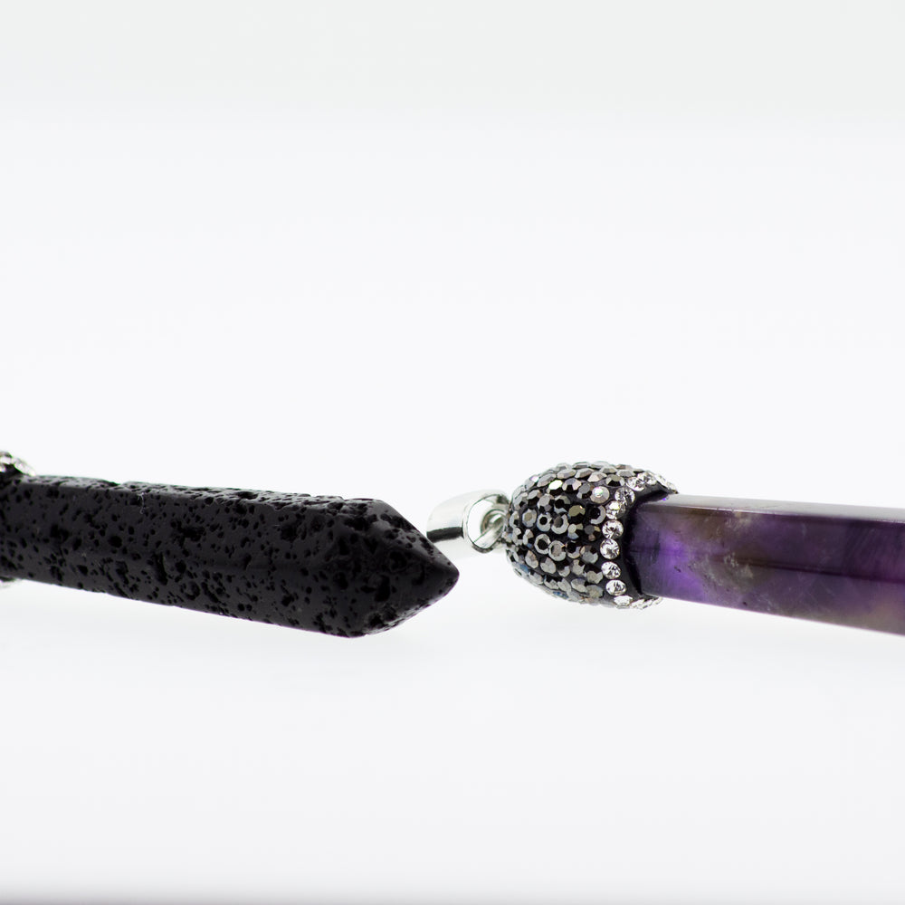 
                  
                    A pair of black and purple lava stones on a white surface, adorned with a turquoise stone and a Super Silver Stone Obelisk Pendant.
                  
                