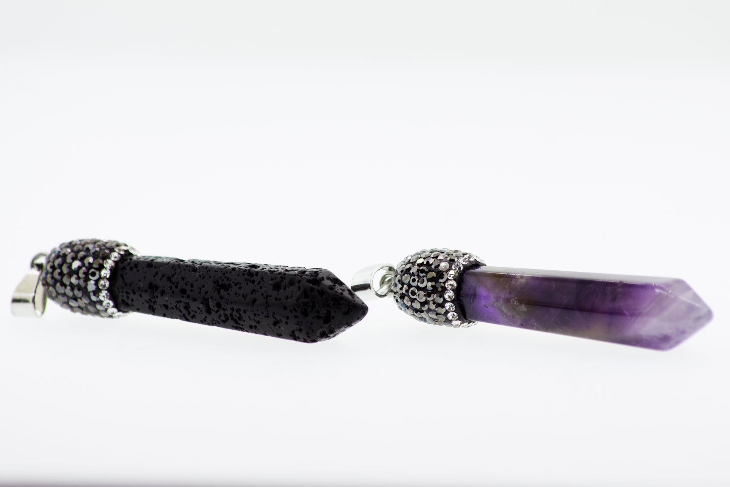 
                  
                    A pair of black and purple lava stones on a white surface, adorned with a turquoise stone and a Super Silver Stone Obelisk Pendant.
                  
                