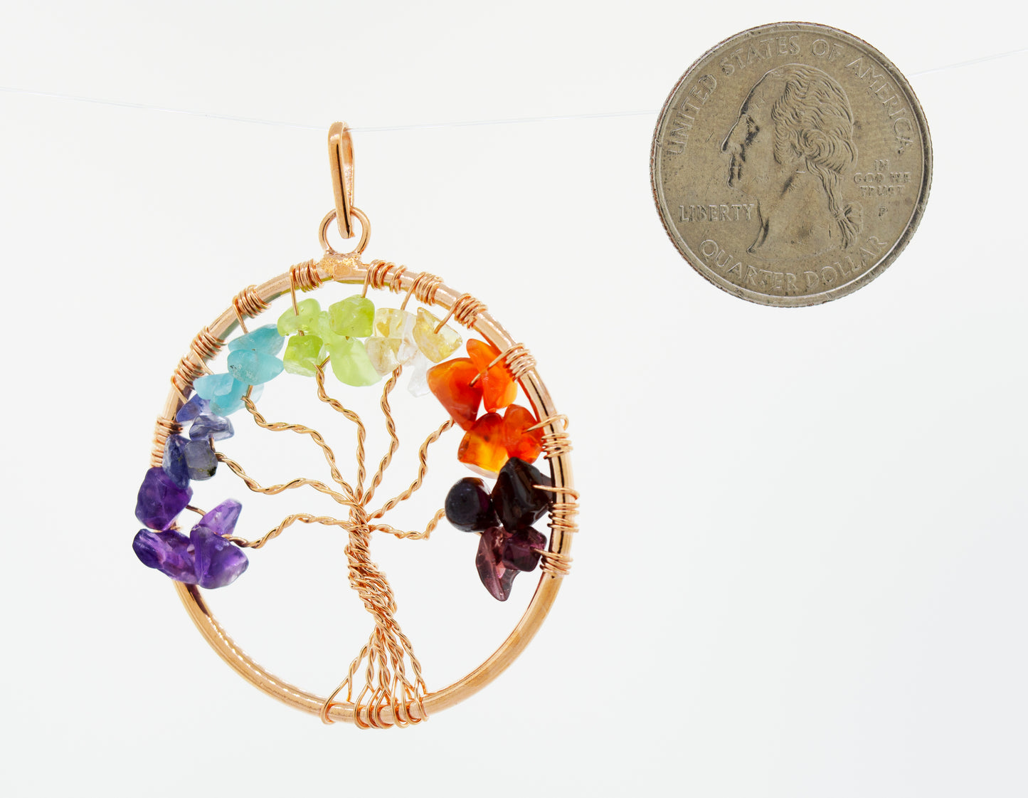 
                  
                    A Super Silver wire-wrapped Chakra Tree of Life pendant adorned with chakra stones, accompanied by a coin.
                  
                