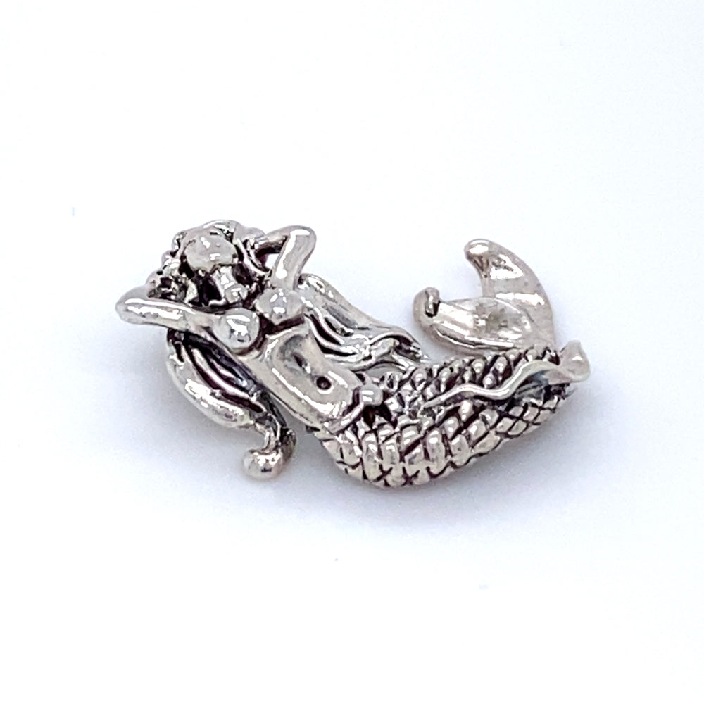 A Super Silver Relaxing Mermaid Charm with Fixed Bail, depicting a mermaid, gracefully rests on a white surface.