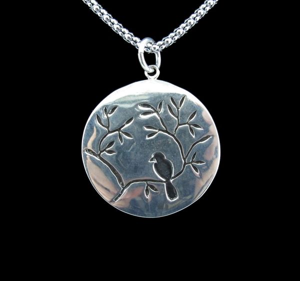 
                  
                    A silver Large Circle Nature Pendant with Bird featuring a bird perched on a branch by Super Silver.
                  
                