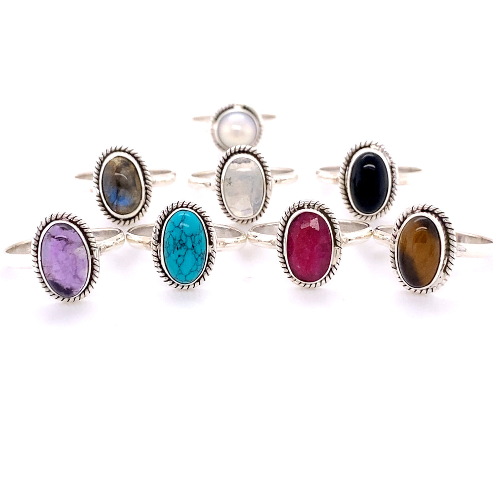 A collection of seven Simple Oval Gemstone Rings with Twisted Rope Border, displayed in a row, featuring stones in various colors including blue, pink, and brown.
