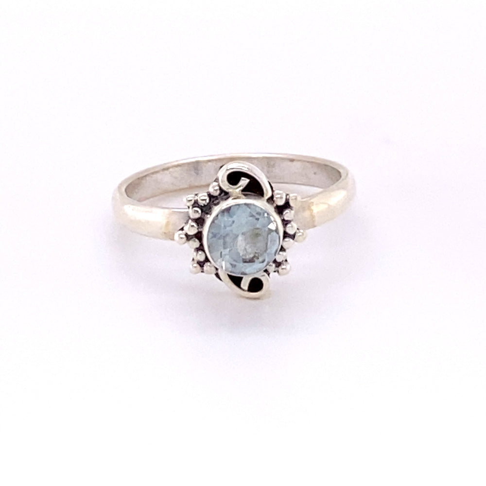 
                  
                    A Small Round Gemstone Ring with Bead and Swirl Border with a blue topaz stone.
                  
                