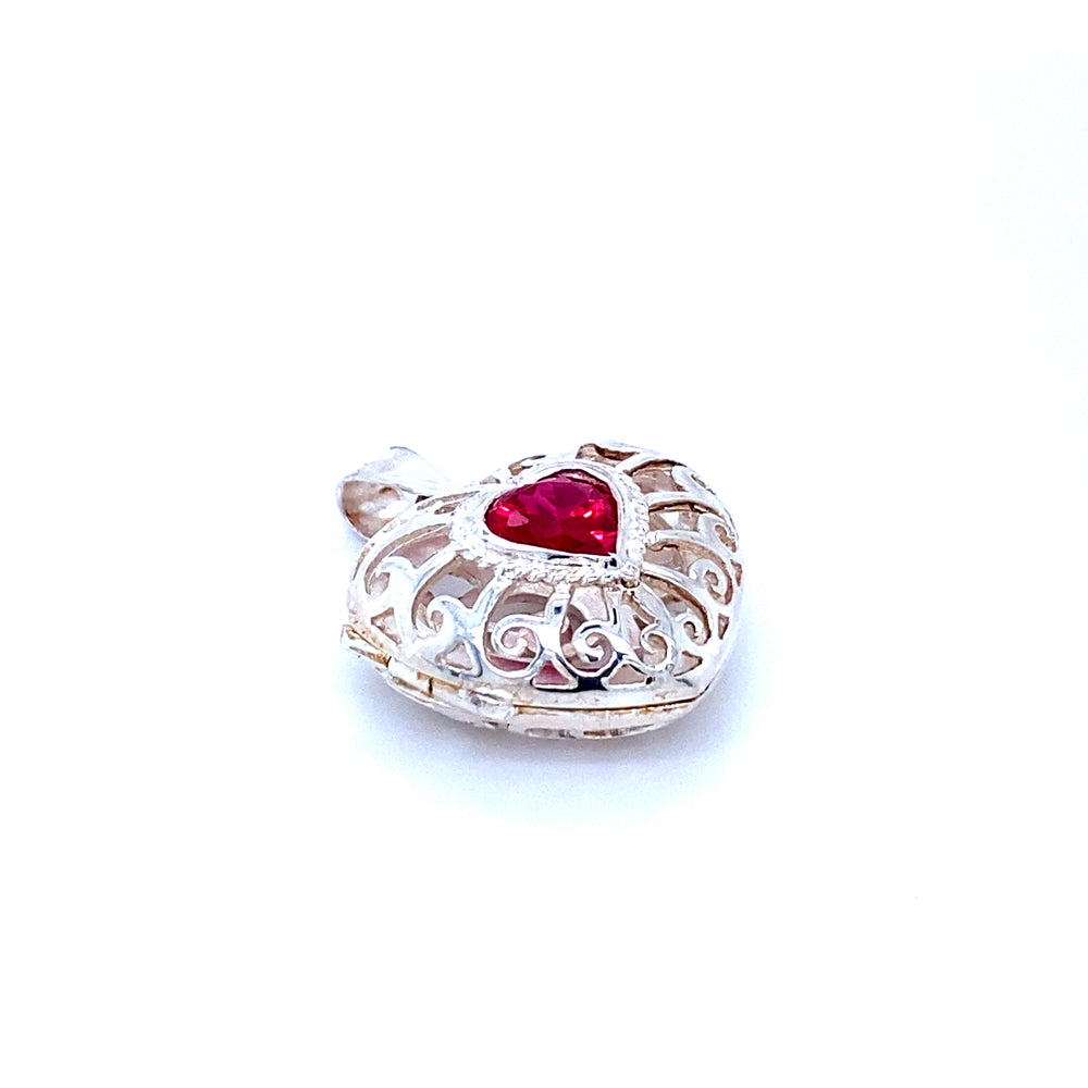 
                  
                    A Super Silver Heart Cage Locket With Cubic Zirconia Stones with a red stone and a delicate filigree design.
                  
                