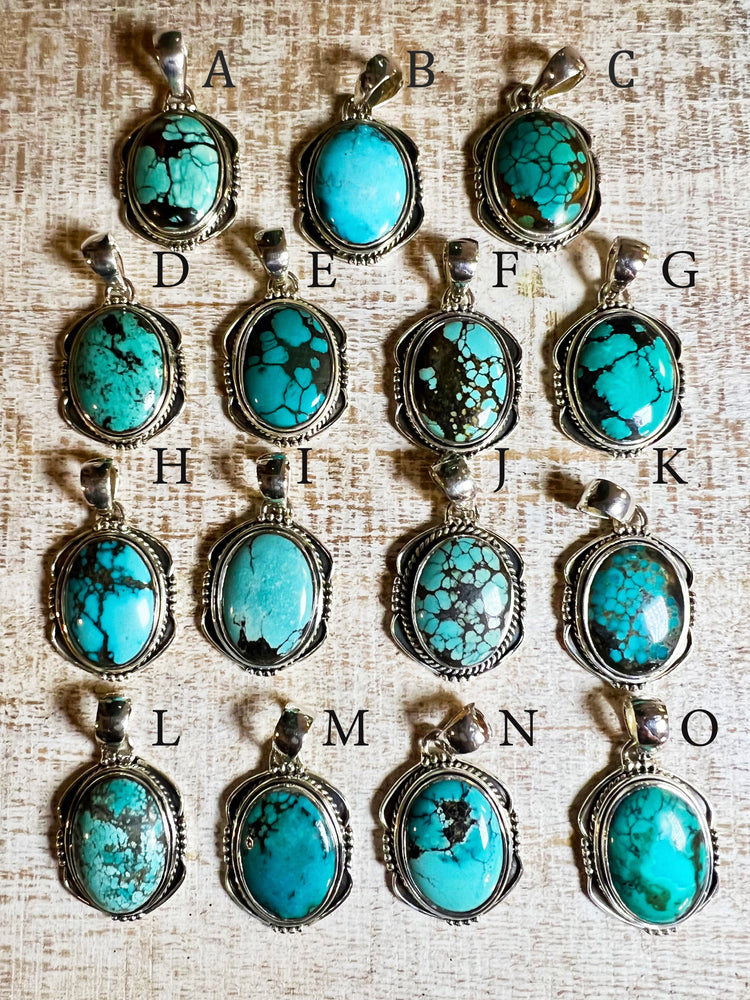 A group of handmade Natural Turquoise Pendants with an Oval Shield Setting from Super Silver on a table.