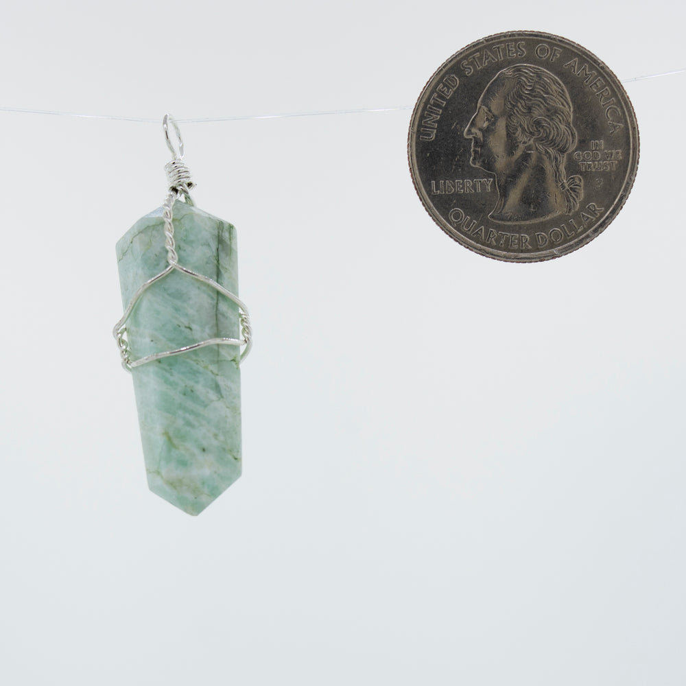 A delicately Super Silver wire-wrapped green jade pendant, made with genuine stone, hanging on a string next to a dime.