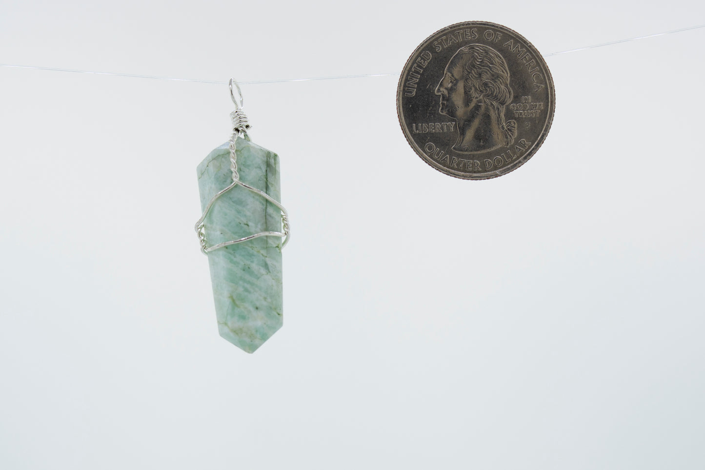 
                  
                    A delicately Super Silver wire-wrapped green jade pendant, made with genuine stone, hanging on a string next to a dime.
                  
                