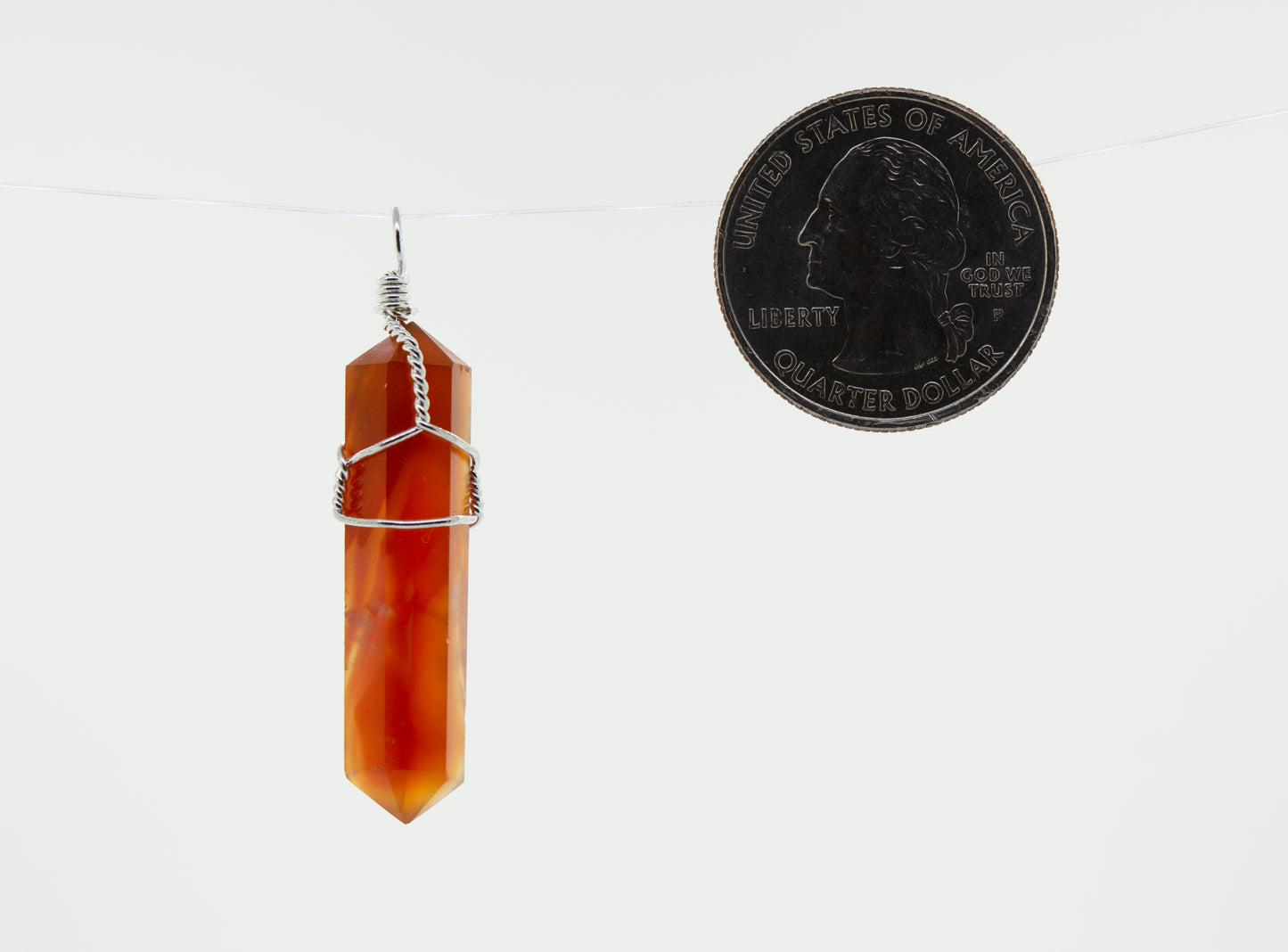 
                  
                    A delicately wire-wrapped Super Silver red agate stone pendant hanging on a string next to a dime.
                  
                