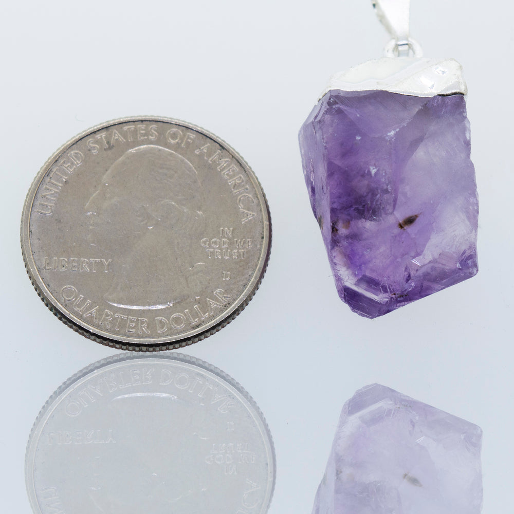 A Natural Amethyst Crystal Pendant showcased in a Super Silver plated setting, next to a dime.