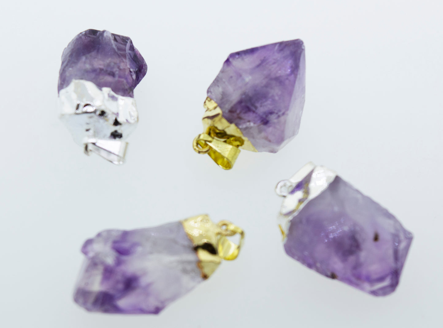 Purple natural amethyst crystals on a white surface enhanced by a Super Silver gold plated setting.