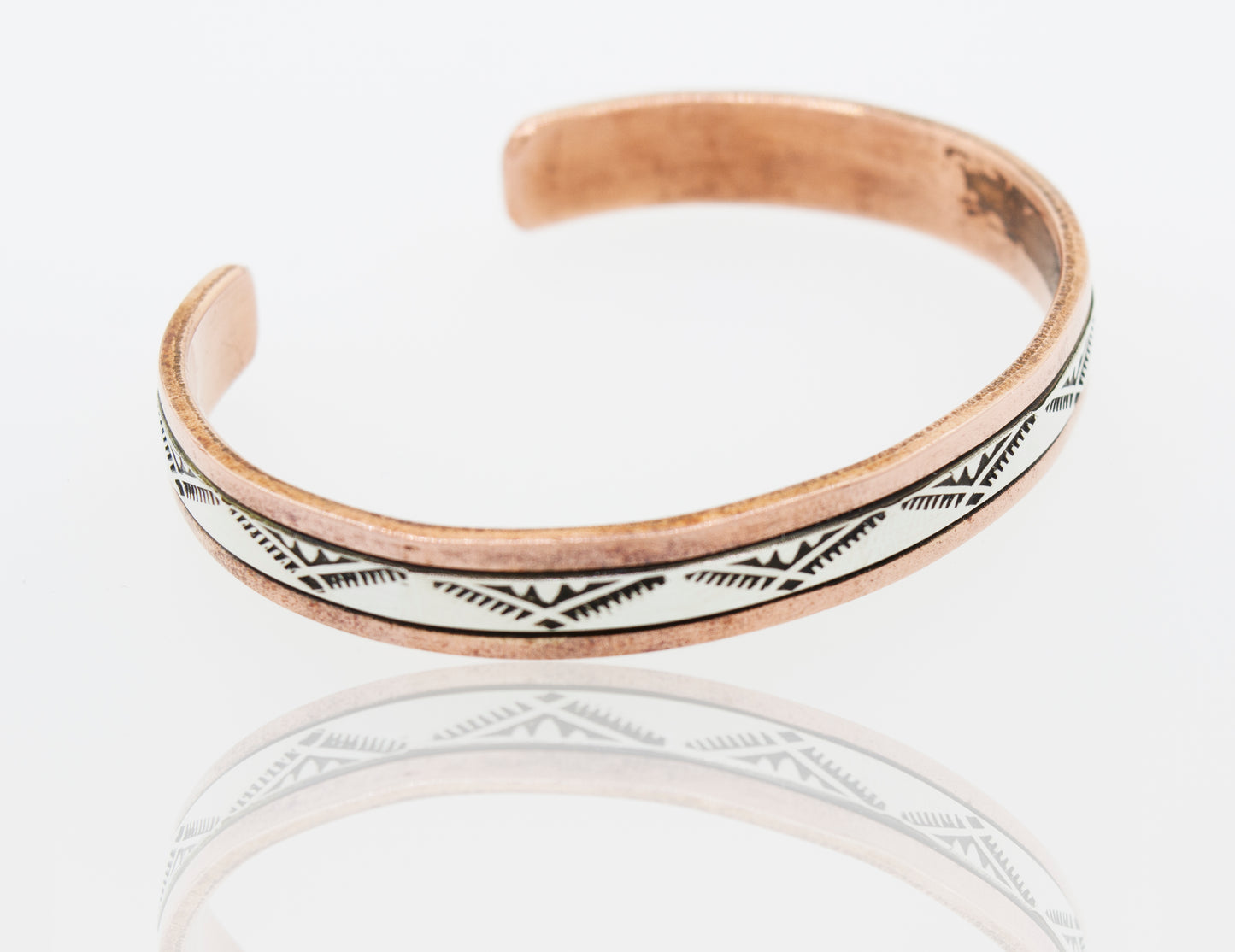 A handcrafted Super Silver Native American copper and silver cuff bracelet adorned with white and black designs.