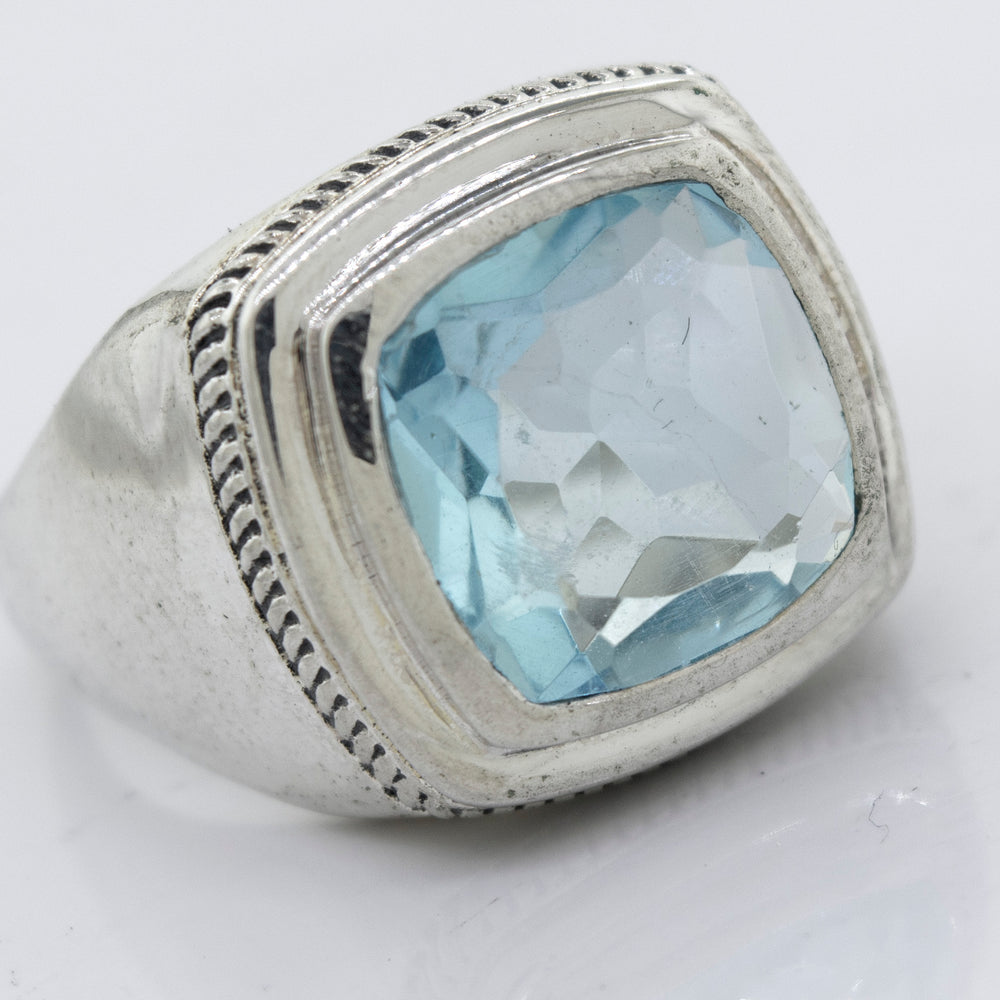 
                  
                    A Faceted Stone Signet Ring with a large, square-cut aquamarine gemstone in the center, featuring detailed engravings around the setting.
                  
                