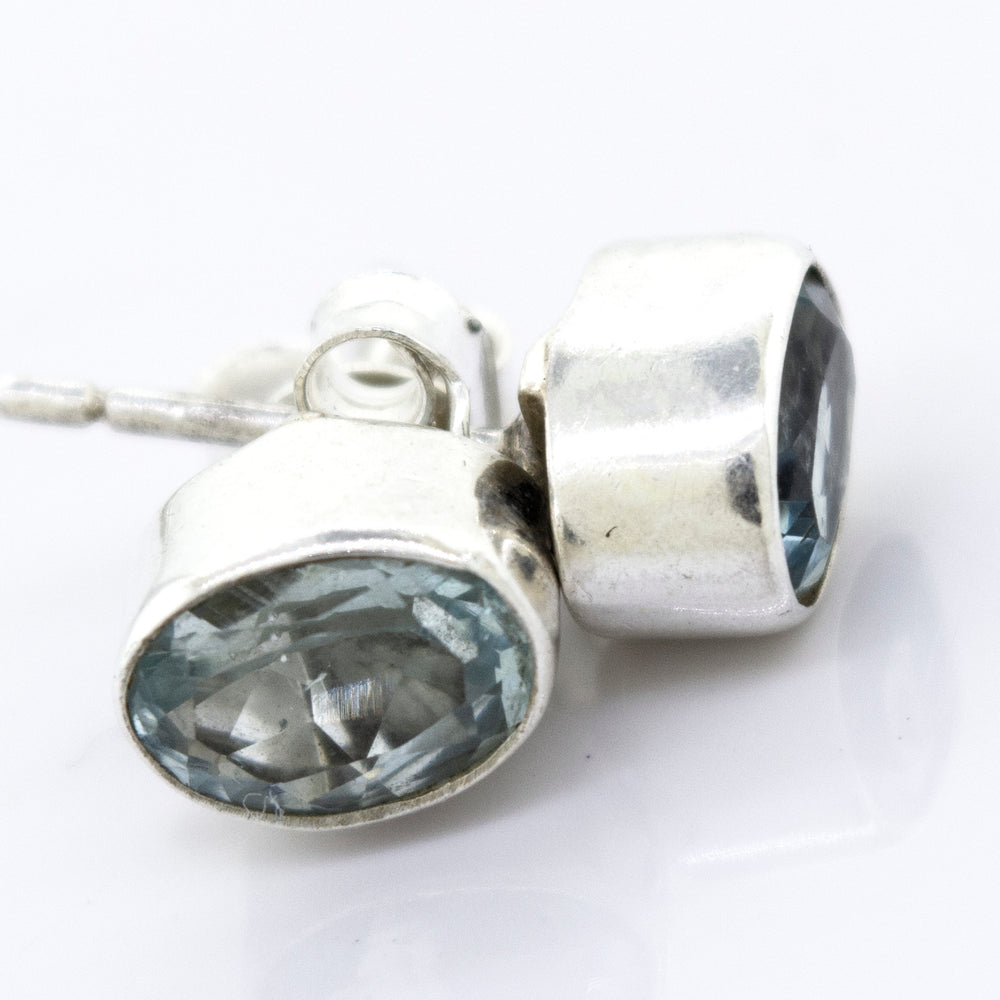 A pair of Beautiful Oval Faceted Cut Blue Topaz Studs from Super Silver in a silver setting on a white surface.