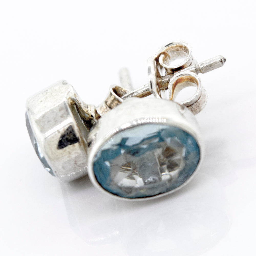 
                  
                    A pair of Beautiful Oval Faceted Cut Blue Topaz Studs with a Super Silver setting on a white surface.
                  
                