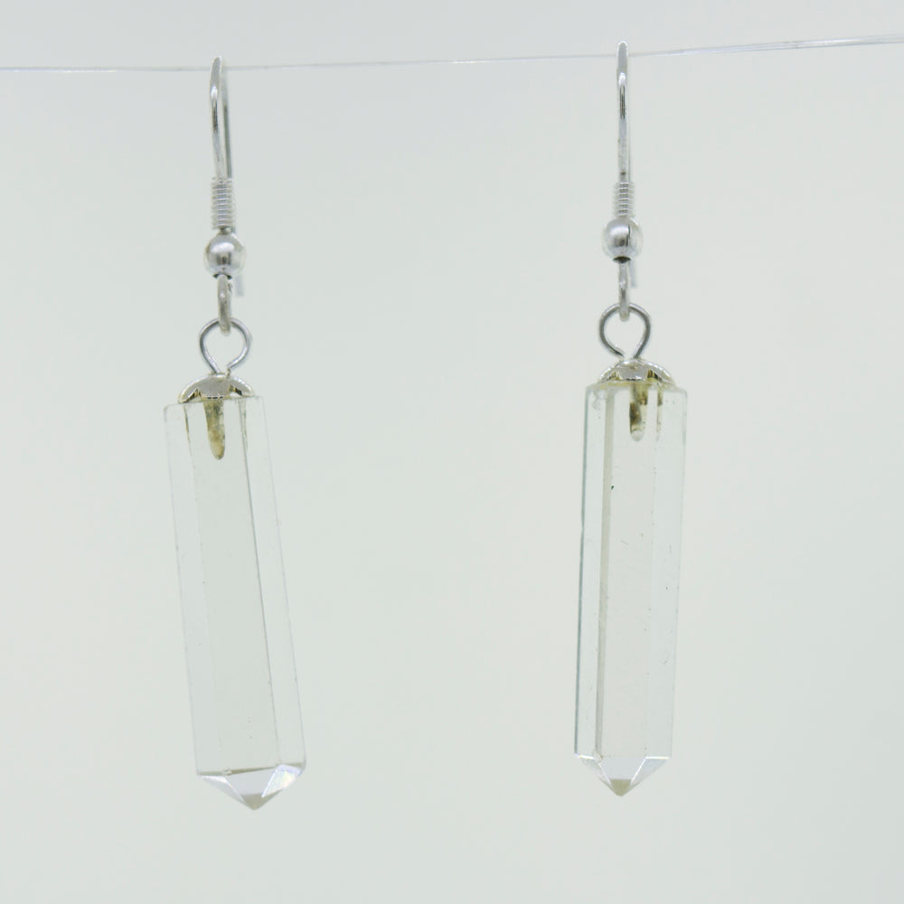 A pair of minimalist Super Silver Raw Stone Earrings in an obelisk shape, hanging from a wire.
