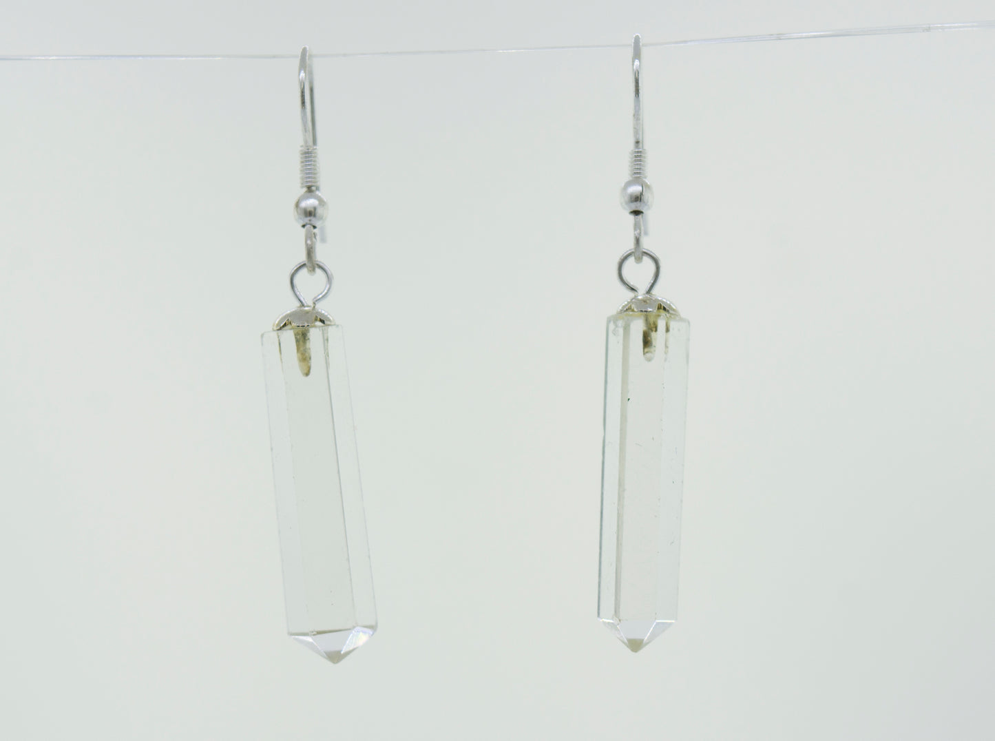 A pair of minimalist Super Silver Raw Stone Earrings in an obelisk shape, hanging from a wire.