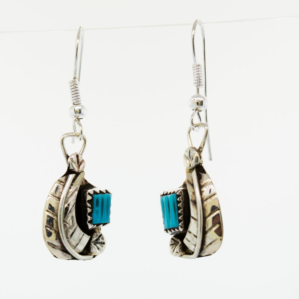A pair of Zuni Handmade Turquoise earrings with a leaf design, hanging from a Super Silver wire.