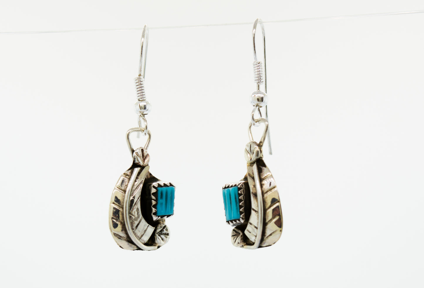 A pair of Zuni Handmade Turquoise earrings with a leaf design, hanging from a Super Silver wire.