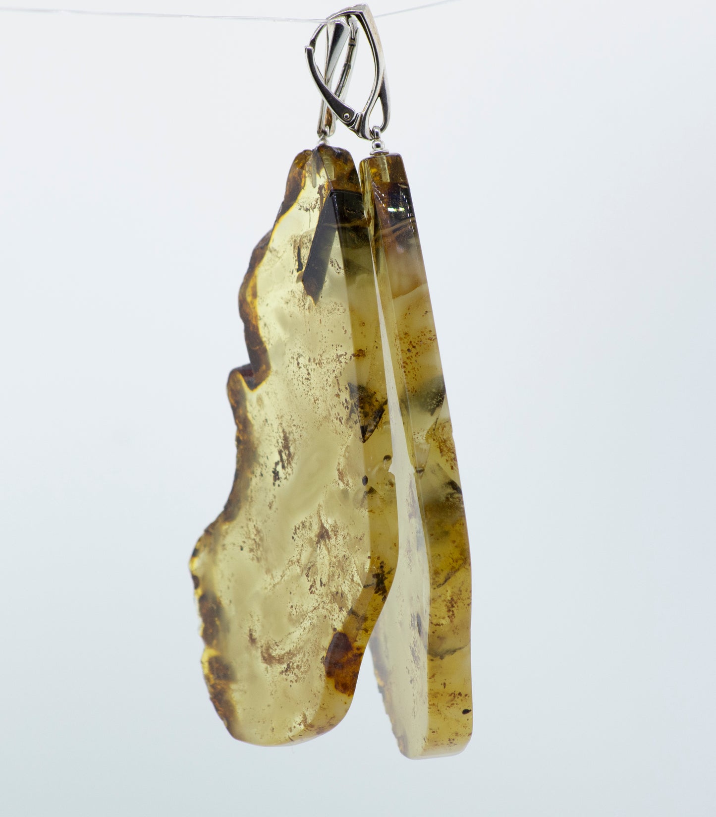 Super Silver Designer Raw Cognac Amber Slab Earrings dangling from a wire.