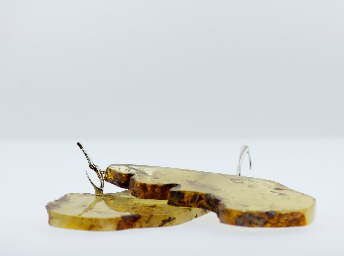 
                  
                    Two Designer Raw Cognac Amber Slab Earrings by Super Silver resting on a white surface.
                  
                