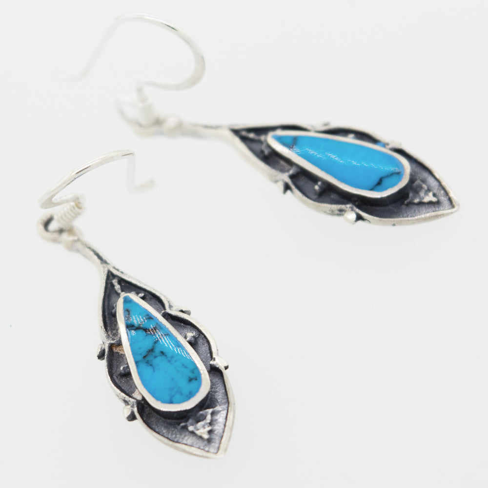 A pair of Super Silver Teardrop Shape Turquoise Earrings adorned with turquoise stones.