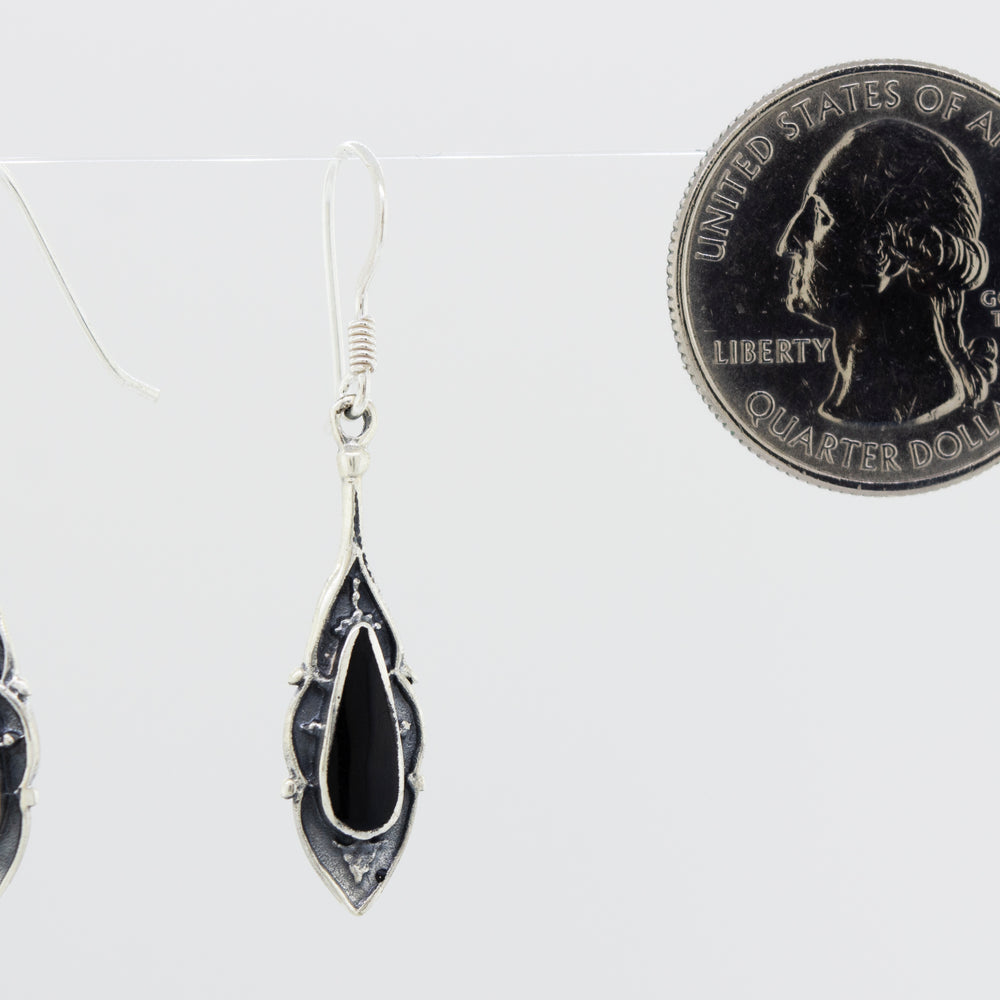 A pair of Super Silver Teardrop Shape Abalone Earrings featuring a black onyx and an oxidized finish, showcased alongside a penny.