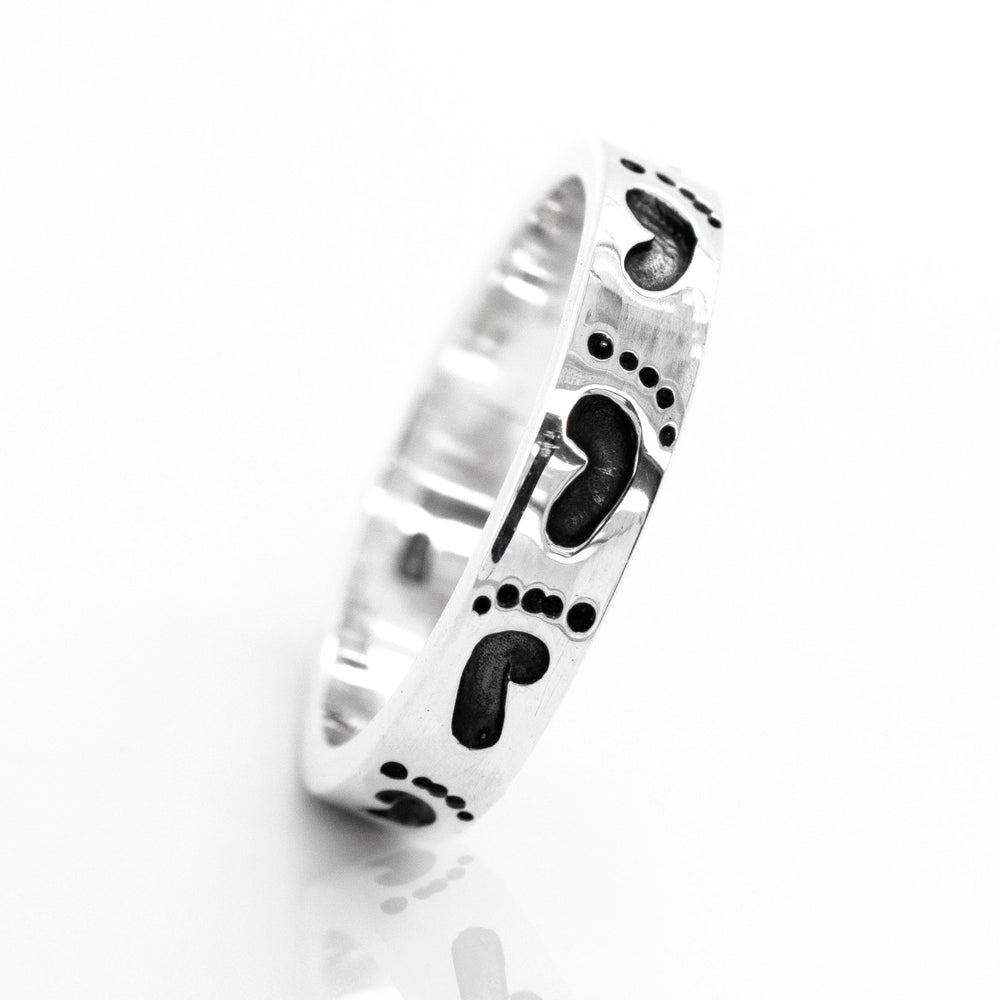 
                  
                    A Super Silver Footprint Band Ring adorned with black footprints, perfect for the beach lover in your life.
                  
                