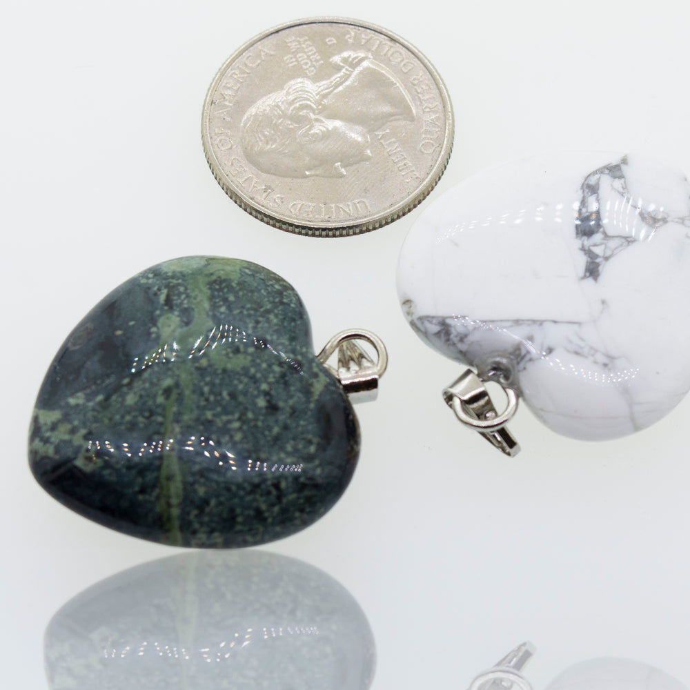 Two Super Silver Heart Stone Pendants, one green and one white, alongside a dime.