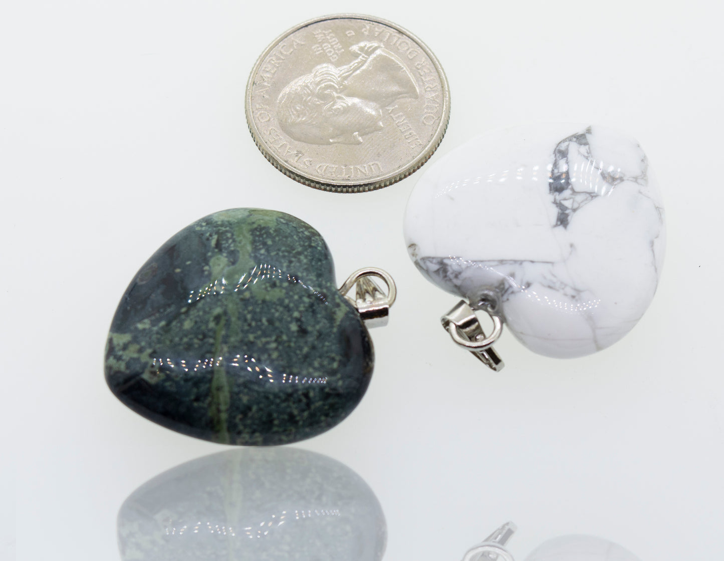 Two Super Silver Heart Stone Pendants, one green and one white, alongside a dime.