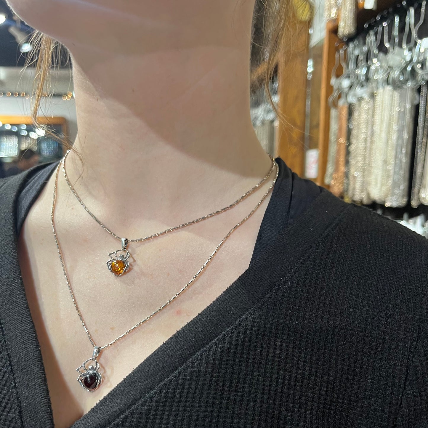 
                  
                    A woman is standing in a jewelry store with two necklaces, showcasing a mesmerizing Delicate Baltic Amber Spider Pendant from Super Silver and an exquisite amber stone. The scene emanates a bewitching aura, evoking a captivating witch.
                  
                