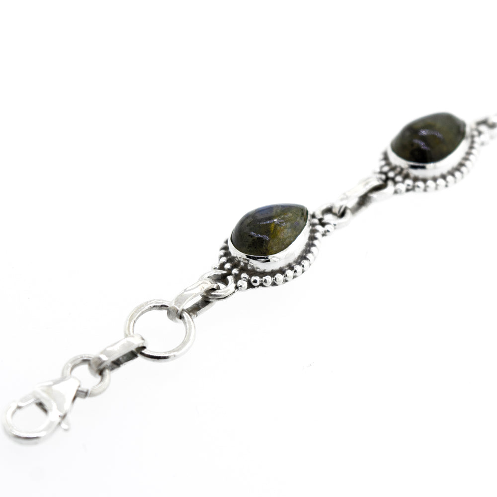 
                  
                    Close-up view of a Teardrop Shape Stone Bracelet With Ball Border adorned with two dark-colored Labradorite stones set in decorative metalwork, featuring a clasp at one end. The bracelet is isolated against a white background.
                  
                