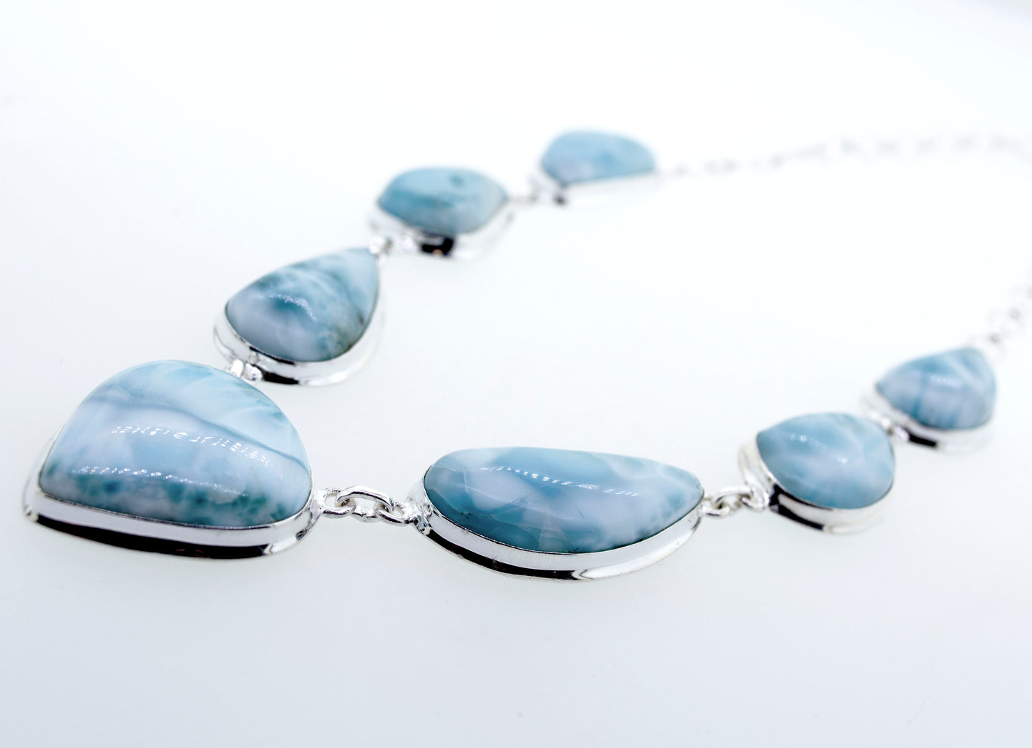 A beautiful Super Silver larimar necklace adorned with raw natural larimar stones in a teardrop shape on a white surface.