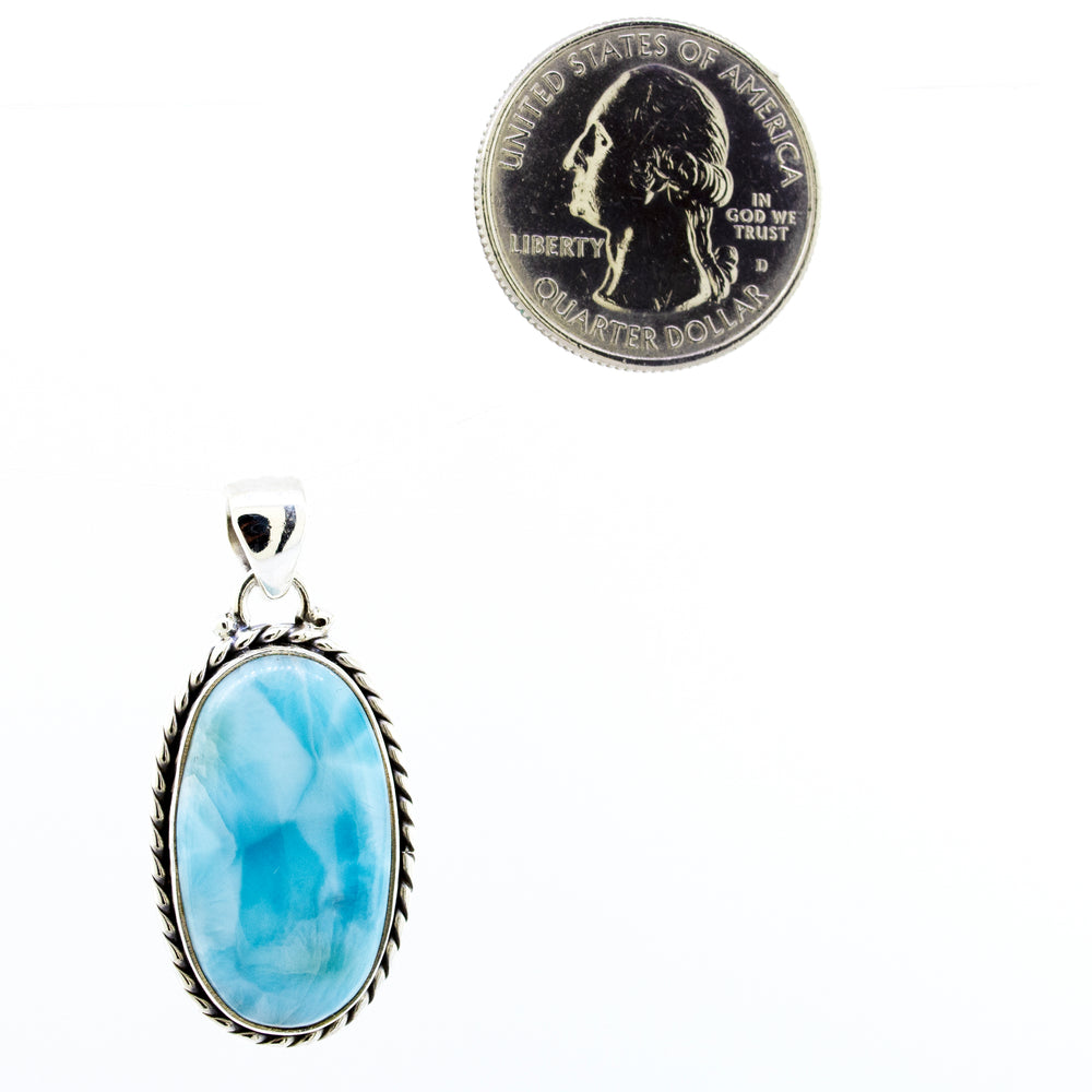 A Medium Larimar Pendant with Special Border made of Sterling Silver with a blue stone resting next to it, by Super Silver.