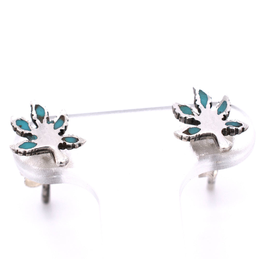 
                  
                    A pair of Super Silver Turquoise Leaf Studs with turquoise stones in the shape of a marijuana leaf.
                  
                