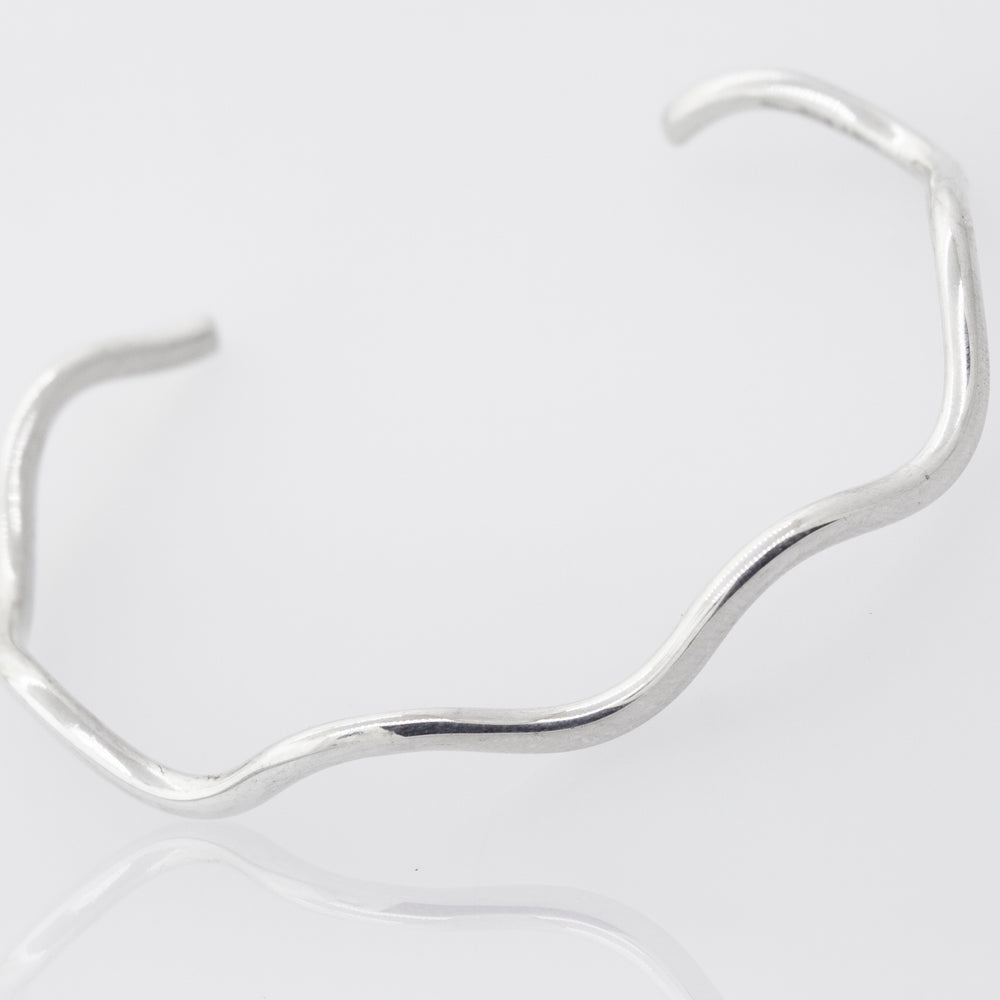
                  
                    A Native American Handmade Silver Wavy Cuff by Super Silver shines bright on a white surface.
                  
                