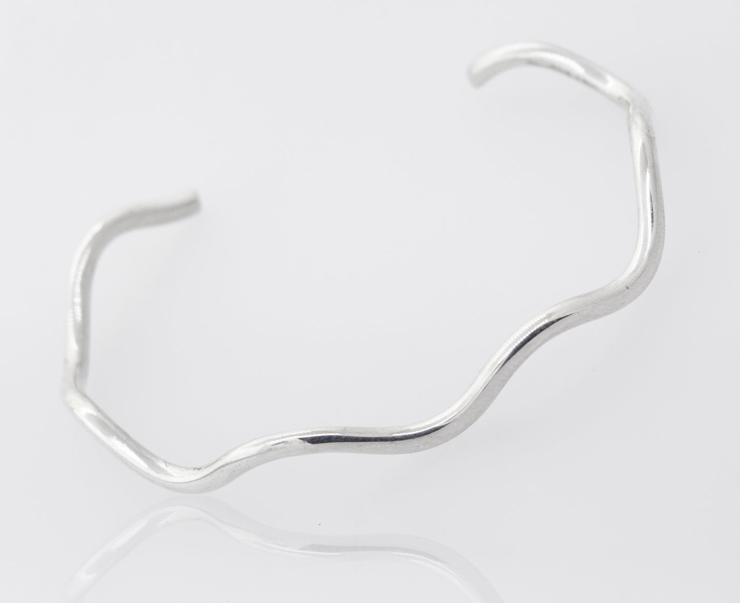 
                  
                    A Native American Handmade Silver Wavy Cuff by Super Silver shines bright on a white surface.
                  
                