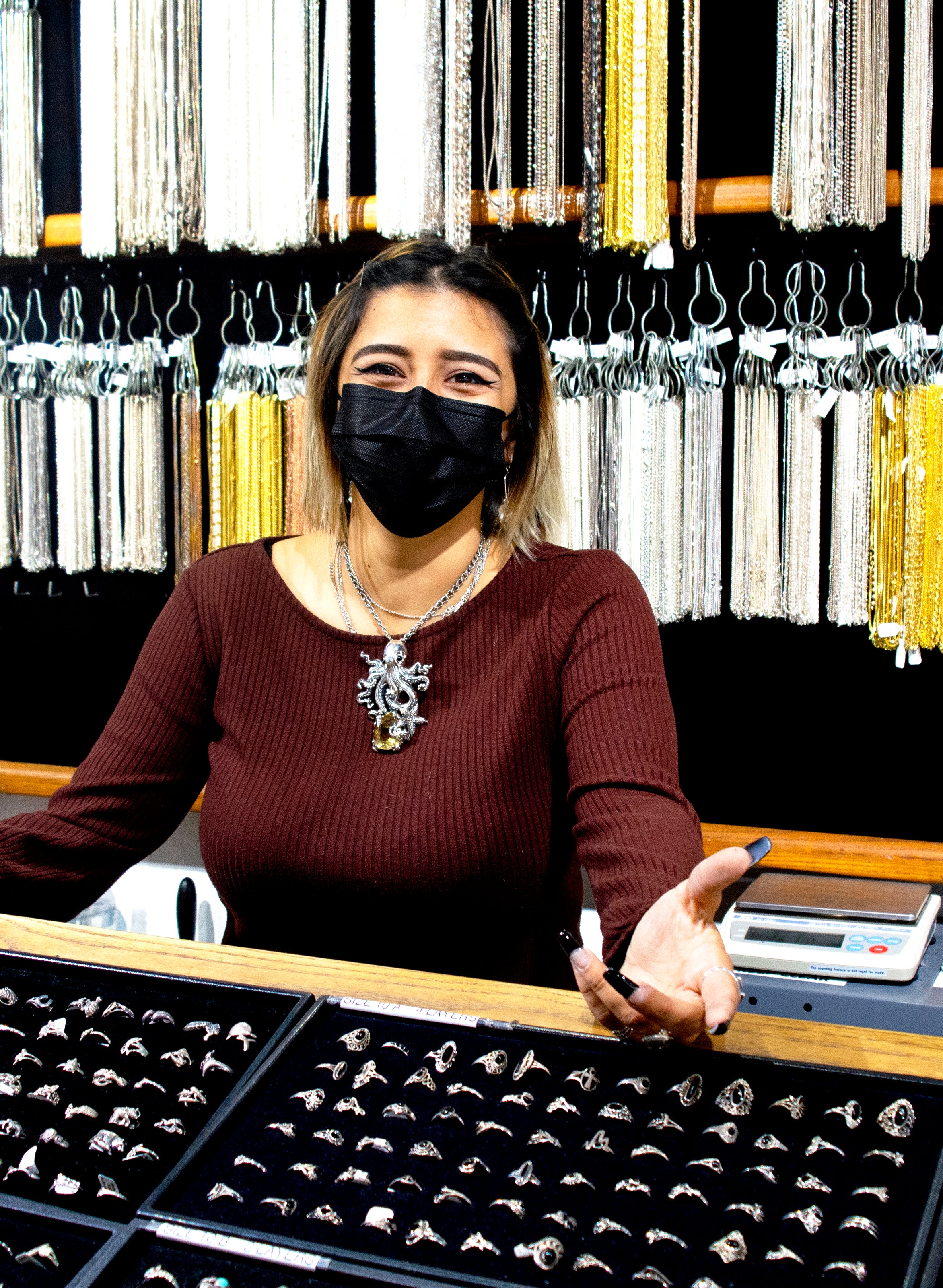 A woman wearing a mask admires a Designer Handmade Octopus Pendant With Vibrant Citrine Crystal from Super Silver in a jewelry store.