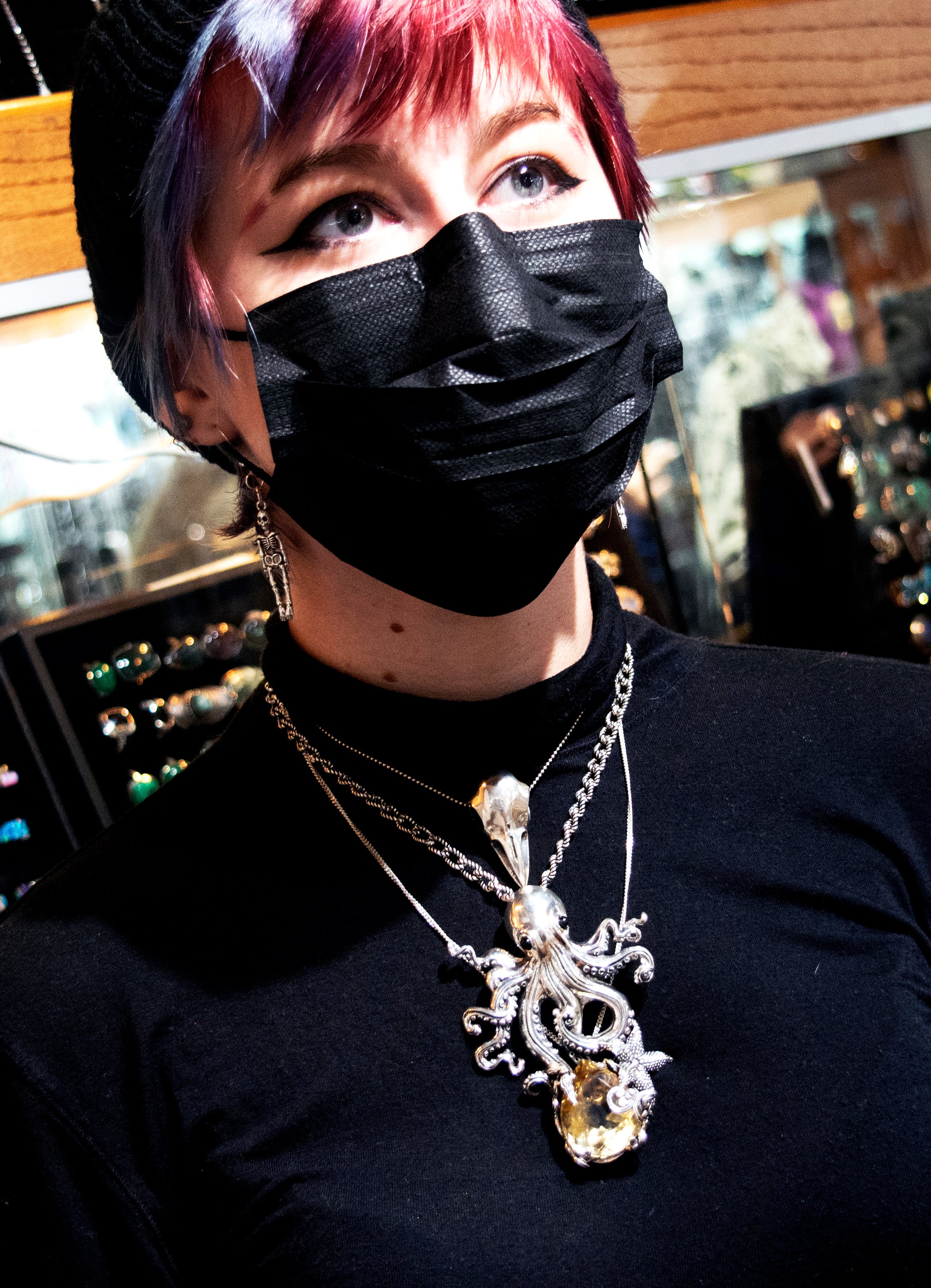 A woman wearing a Super Silver Designer Handmade Octopus Pendant With Vibrant Citrine Crystal mask in a jewelry store.