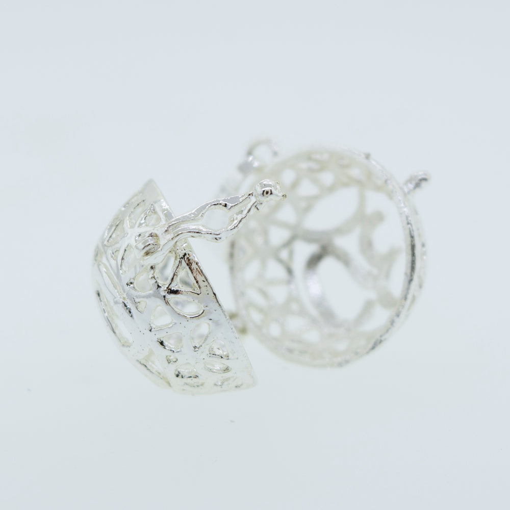 
                  
                    A pair of Super Silver Om Cage Pendant earrings on a white surface.
                  
                