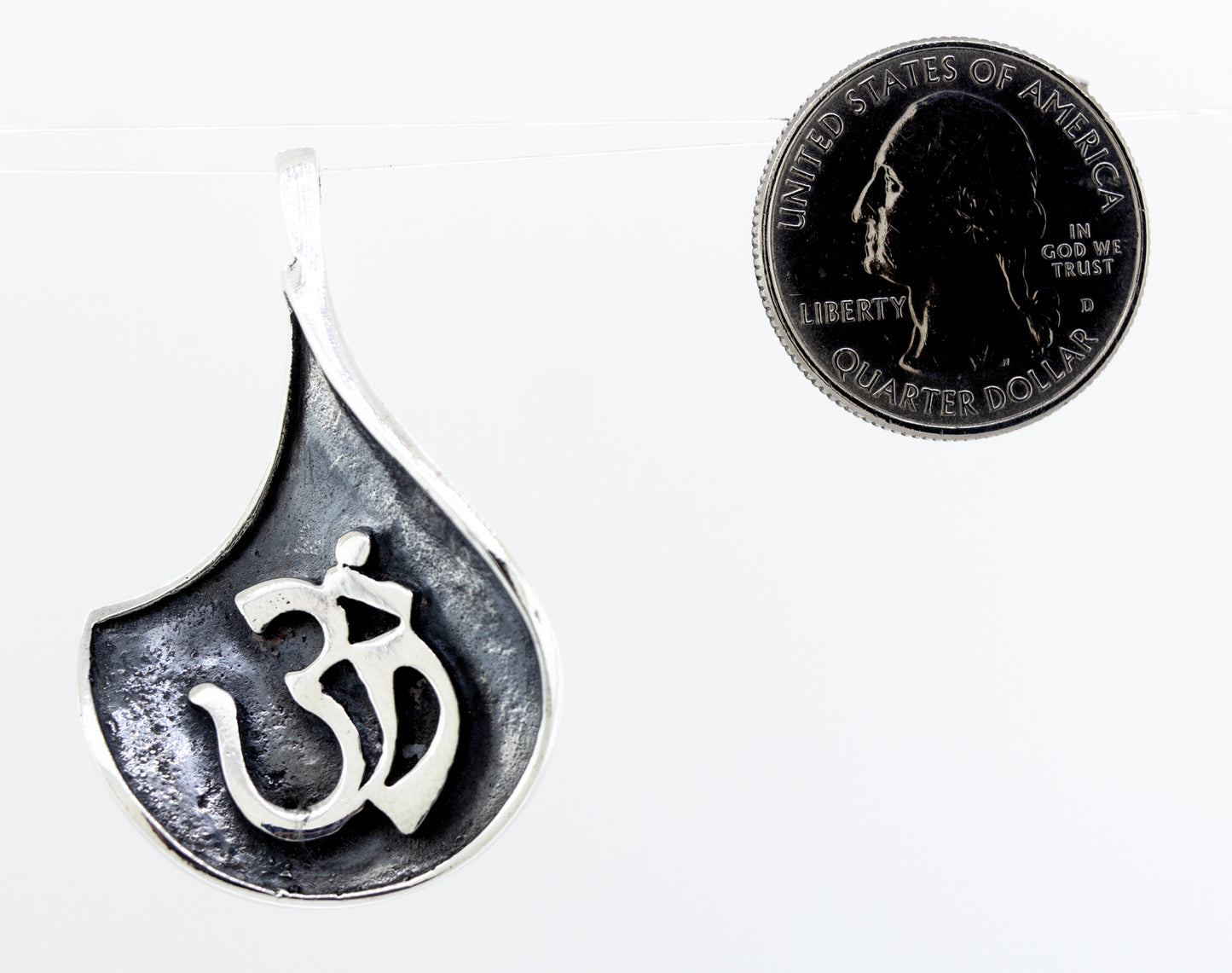 
                  
                    A Super Silver Om Symbol Pendant with an oxidized finish, accompanied by a coin.
                  
                