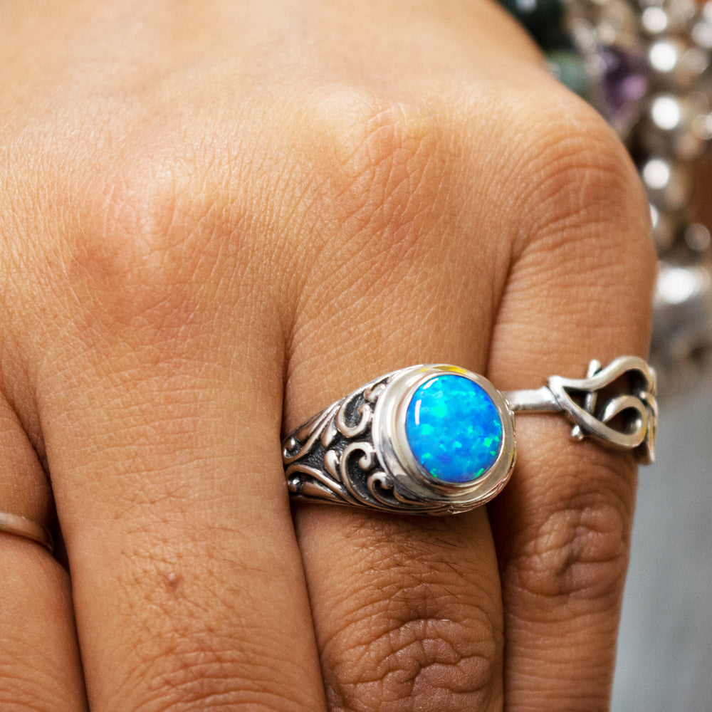 
                  
                    Close-up of a hand wearing rings with various designs, featuring a prominent Opal Signet Ring with Bali Design.
                  
                