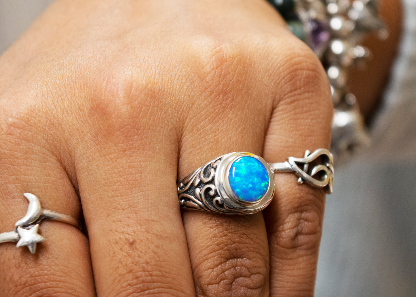 
                  
                    Close-up of a hand wearing rings with various designs, featuring a prominent Opal Signet Ring with Bali Design.
                  
                