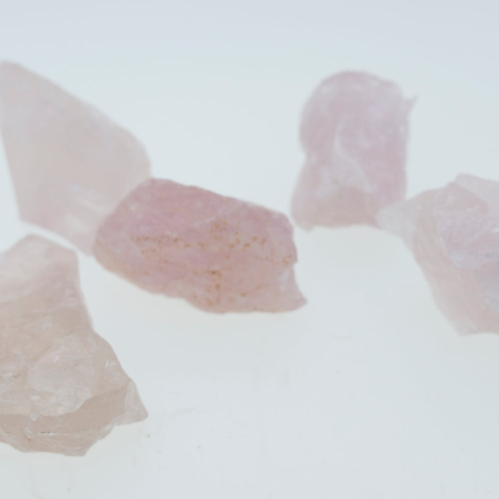 A group of raw rose quartz crystals on a white surface, perfect for decorating any space.