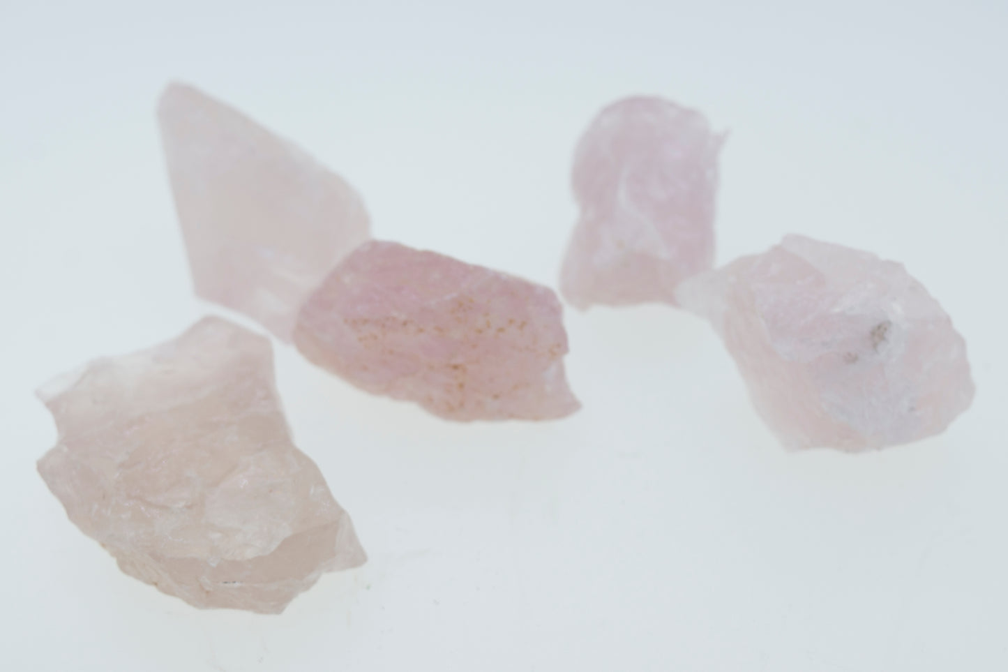 A group of raw rose quartz crystals on a white surface, perfect for decorating any space.