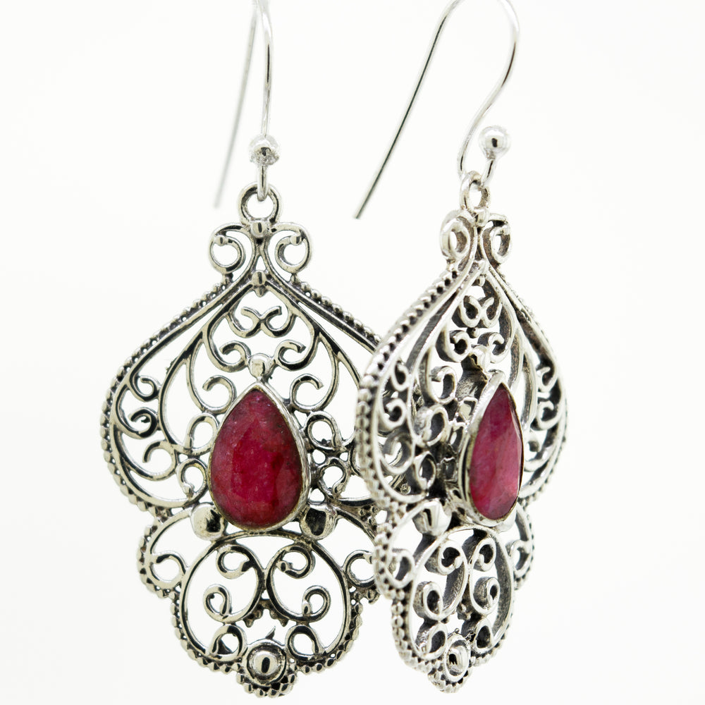 A pair of Teardrop Ruby Earrings With Freestyle Silver Design by Super Silver, featuring a vibrant teardrop-shaped ruby stone, set in a silver setting.