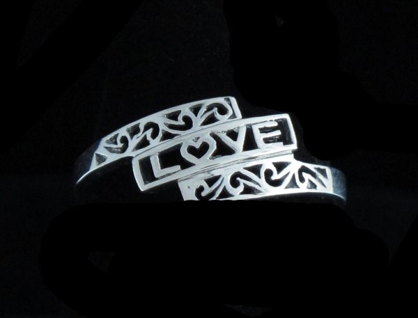 Two intricately designed "Love" Ring Framed with Filigree with the word "LOVE" engraved, set against a dark background.