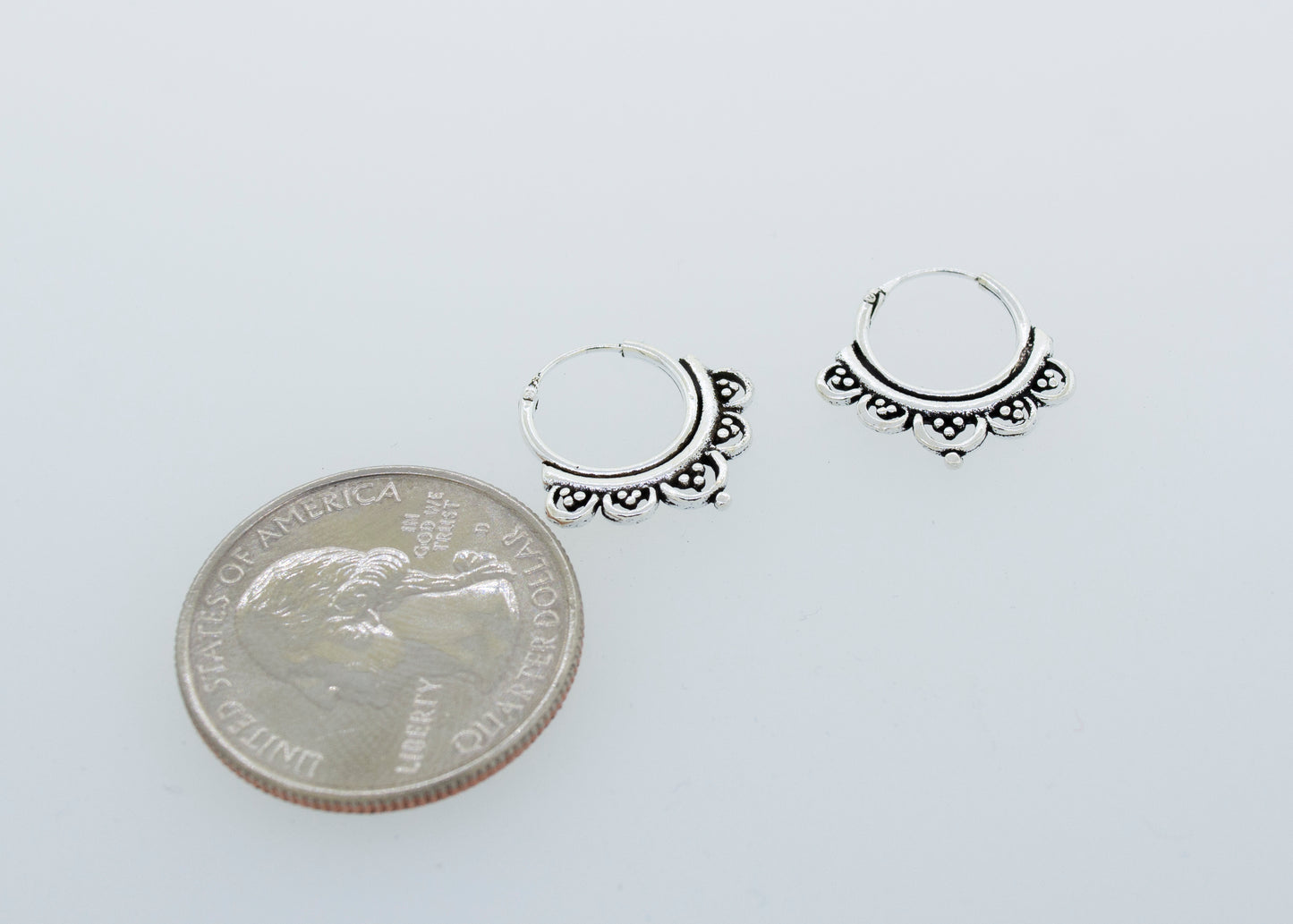 A pair of Super Silver Small Beautiful Freestyle Hoop Earrings next to a quarter.