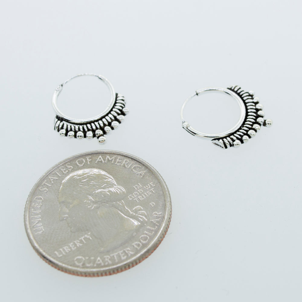 
                  
                    A pair of Small Freestyle Rope and Ball Hoop Earrings made by Super Silver delicately balanced on top of a quarter.
                  
                